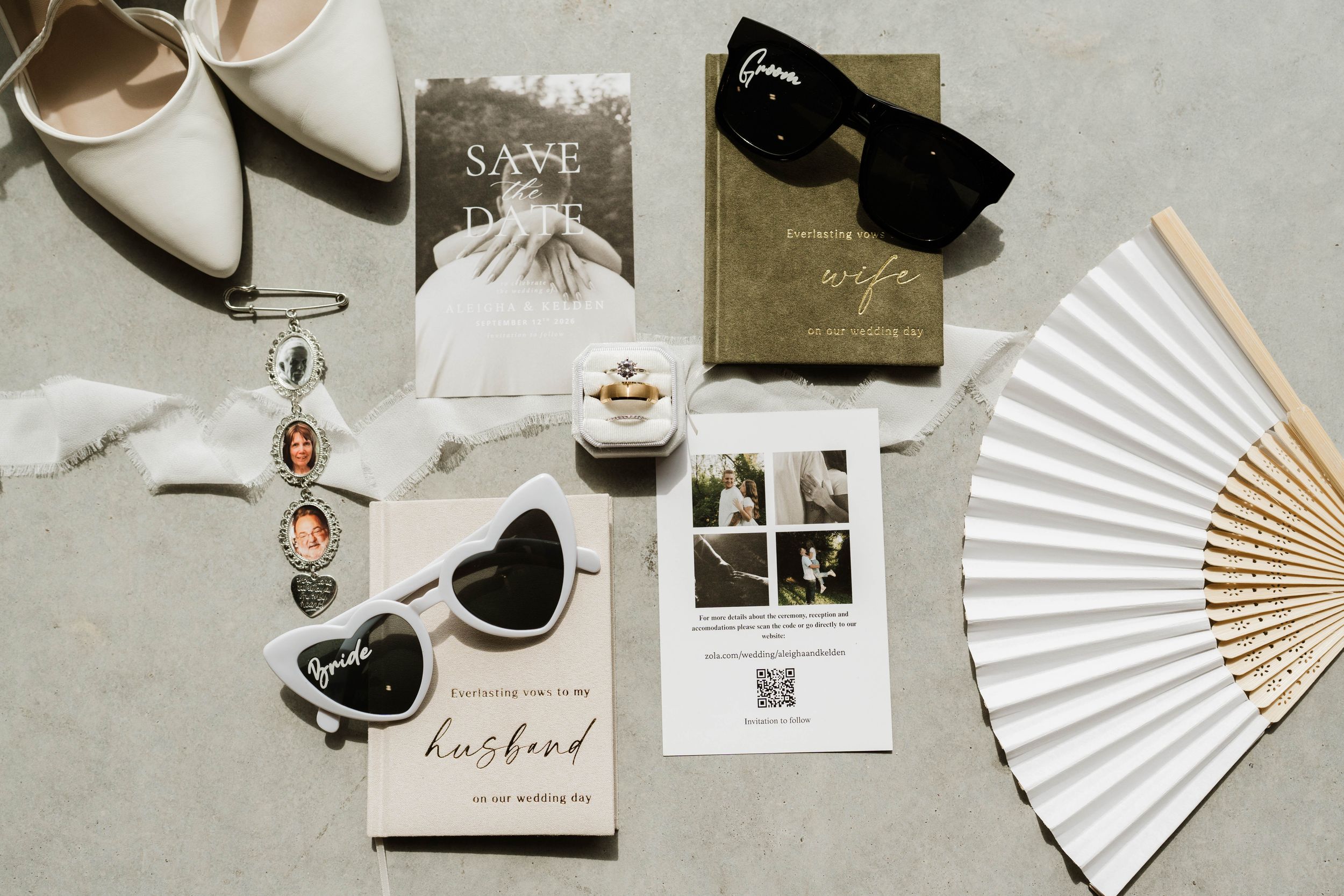 Elegant wedding flat lay with save the date card, sunglasses, ring, fan, photos, and bridal accessories on gray surface.