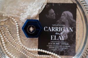 Wedding invitation for Carrigan and Elay on a silver tray with pearl necklace and navy blue hexagon ring box.