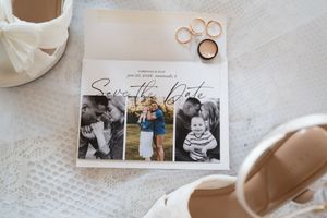 Wedding save the date card with couple photos, gold rings, and bridal heels on a white lace background.