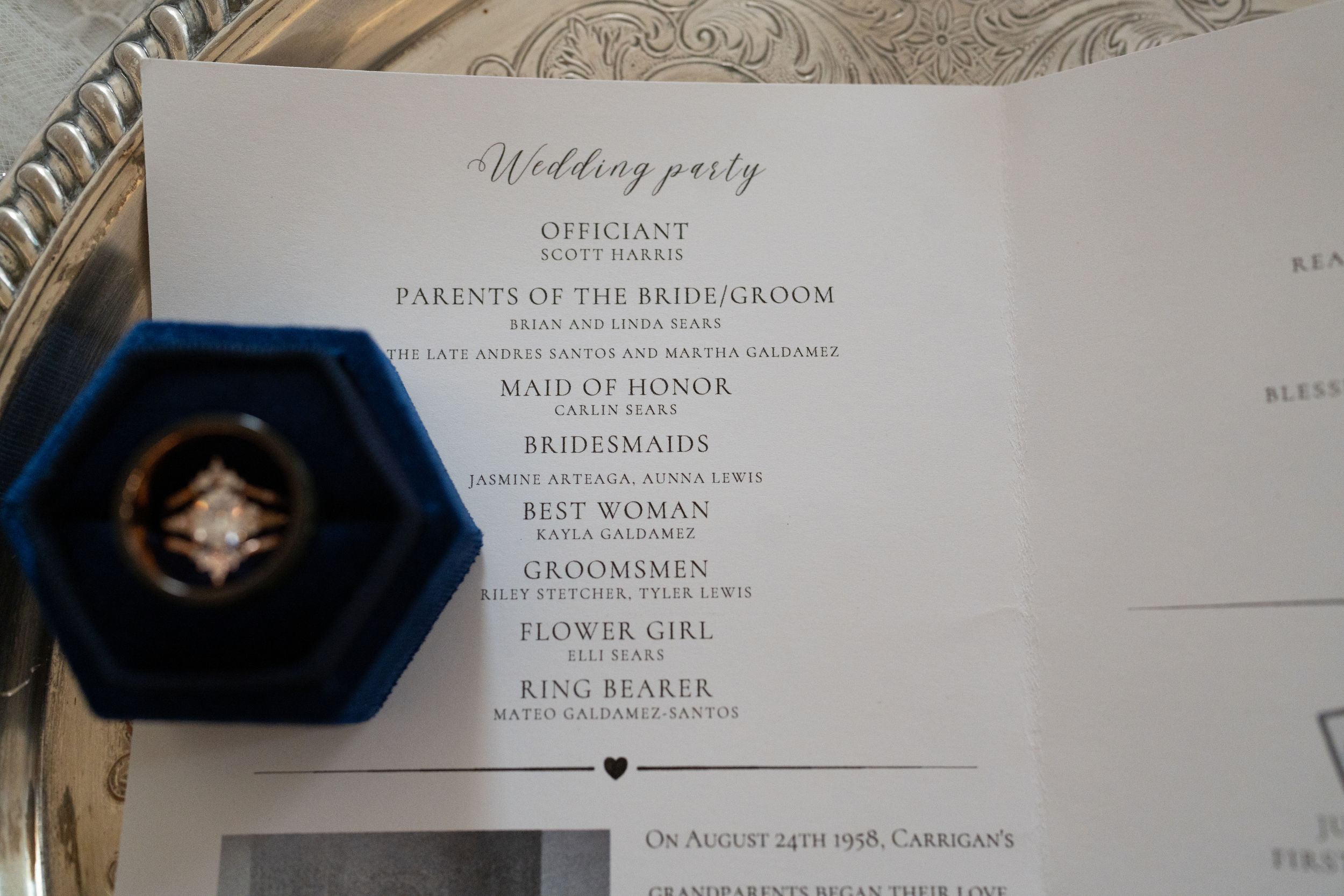 Elegant wedding party program on silver tray with blue velvet ring box and diamond engagement ring.