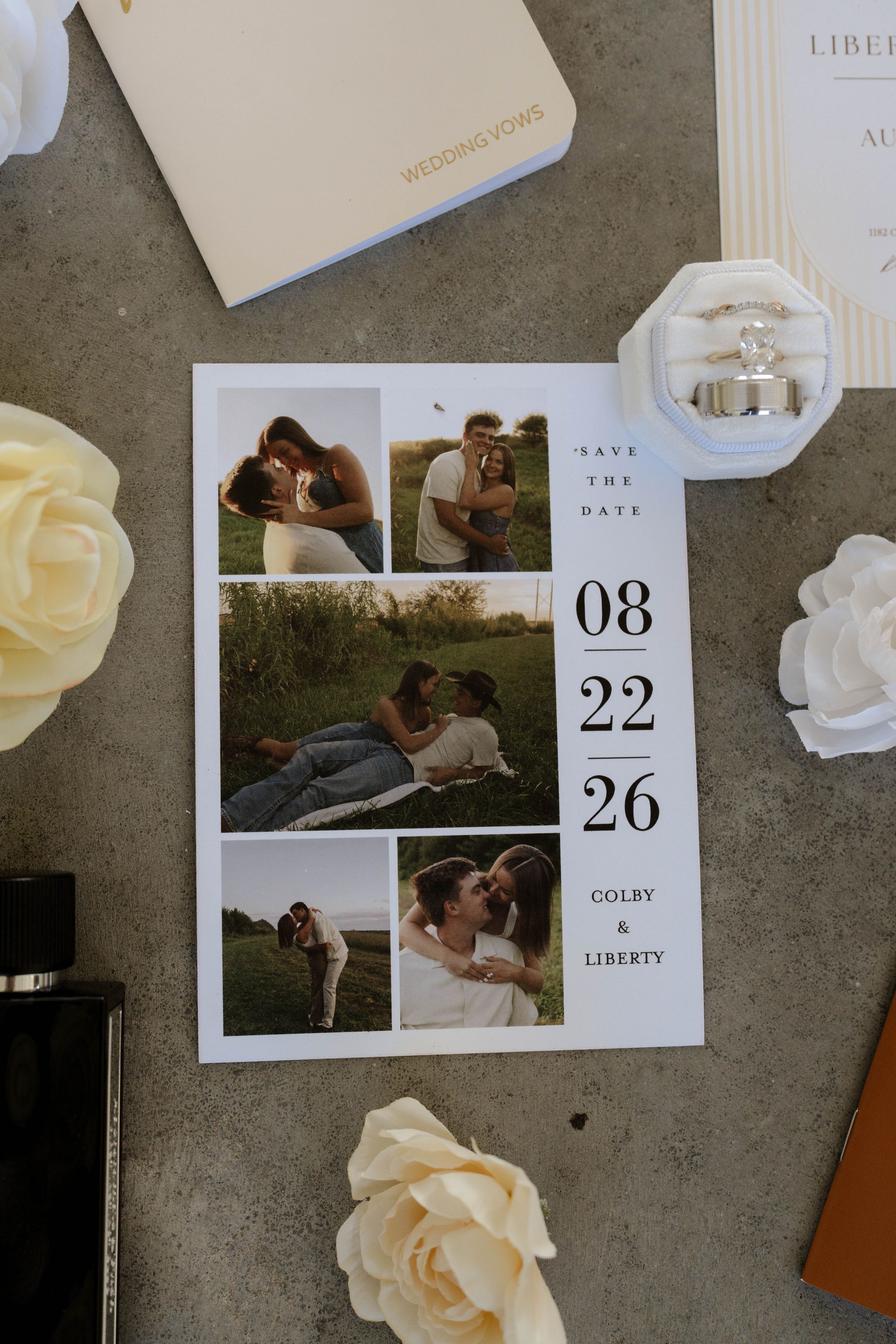 Save the date card for Colby and Liberty on 08/22/26, featuring engagement photos, roses, and wedding rings on a gray surface.
