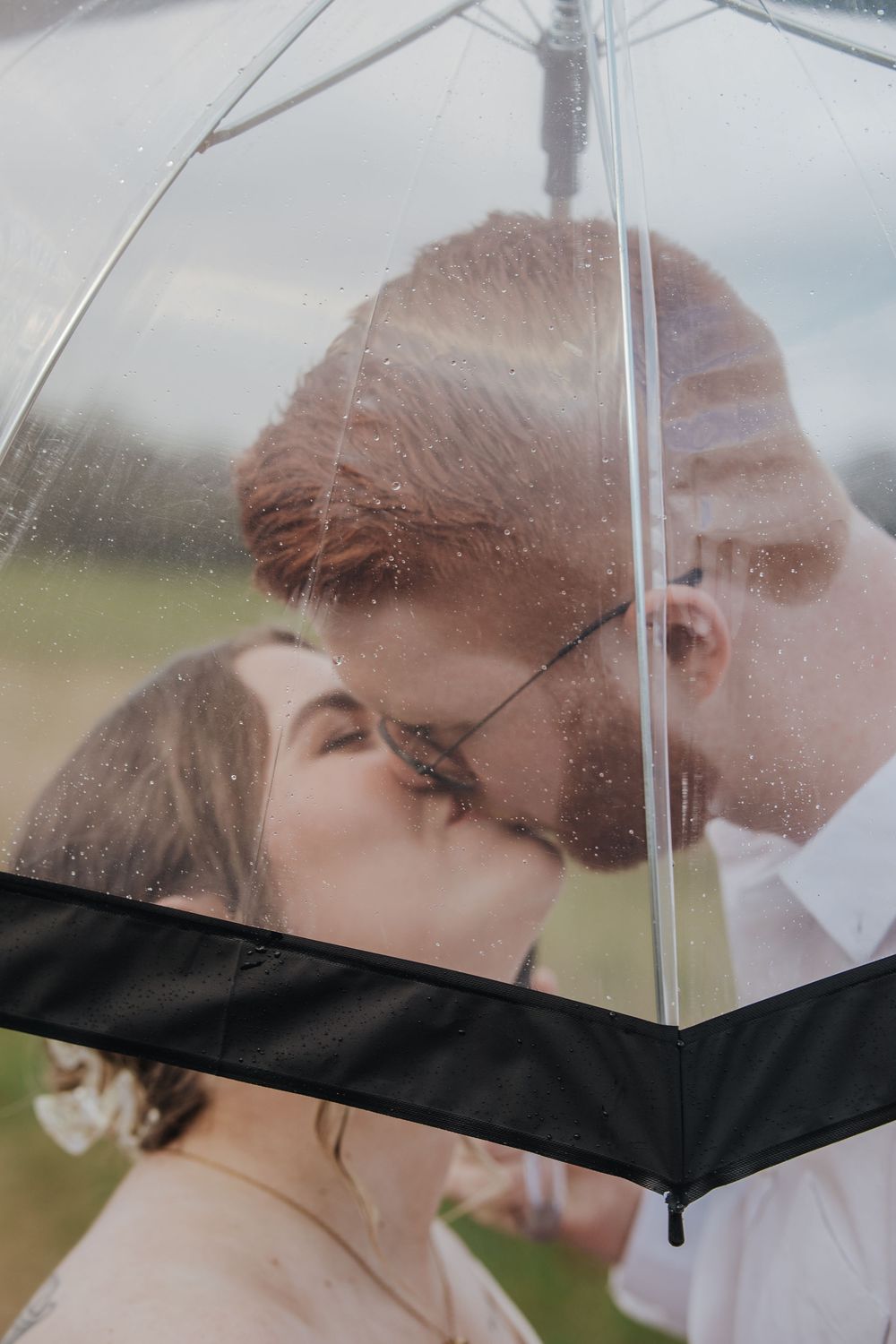 Couple kissing romantically under a clear umbrella in the rain, captured through the wet transparent canopy.