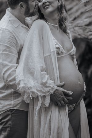 Black and white maternity photo of a couple, man kissing woman's cheek while cradling her pregnant belly.