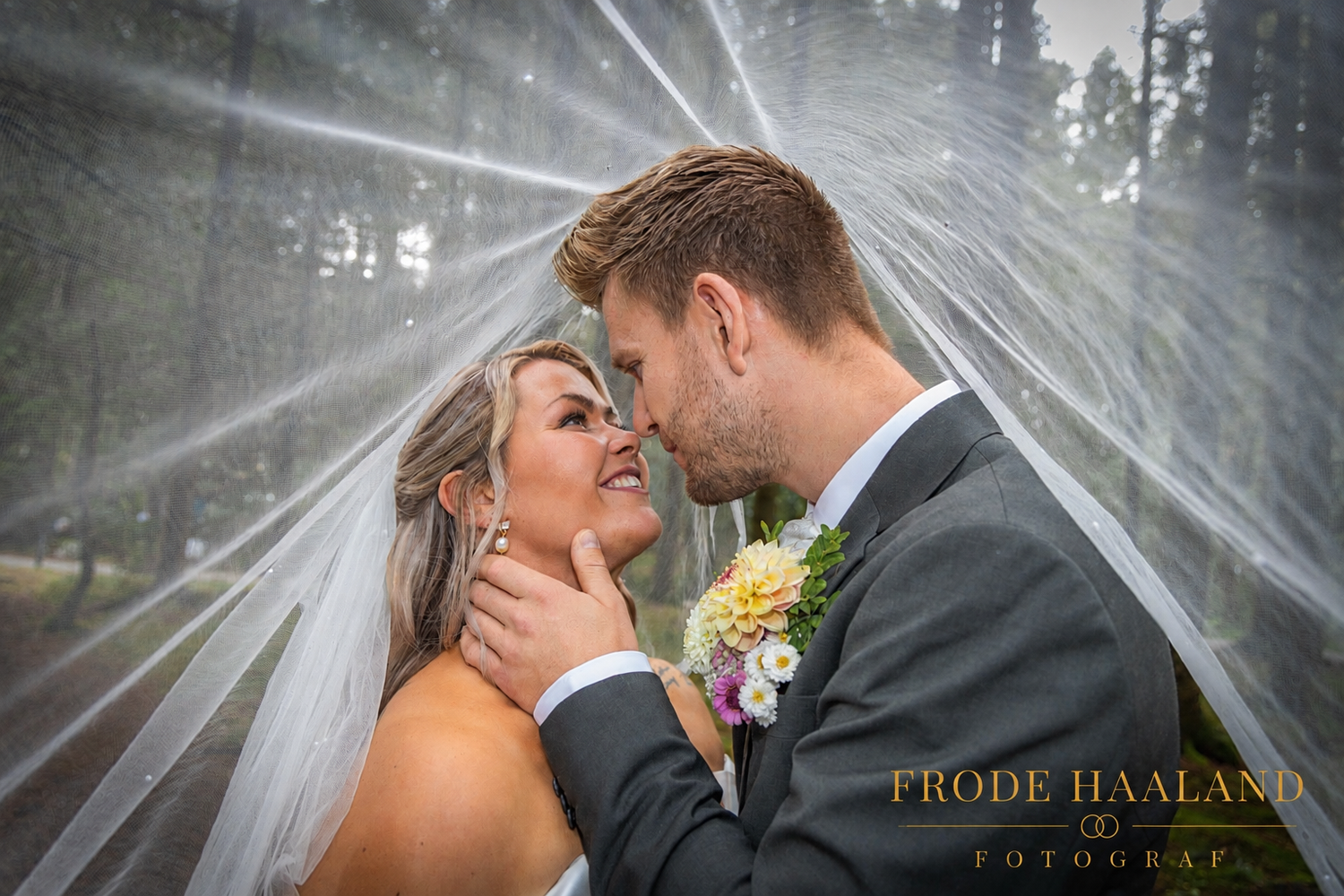Bride and groom share a romantic moment under a flowing veil, surrounded by trees, captured by Frode Haaland Fotograf.