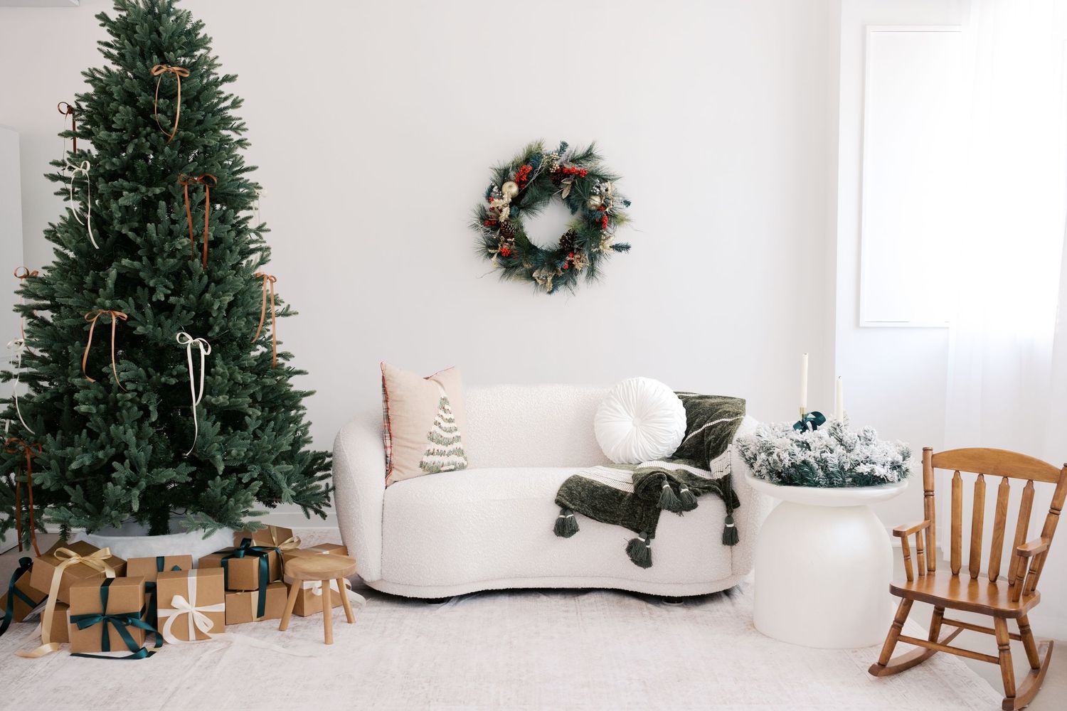 Festive living room with decorated Christmas tree, wrapped gifts, wreath, white sofa, and rocking chair in bright white space.