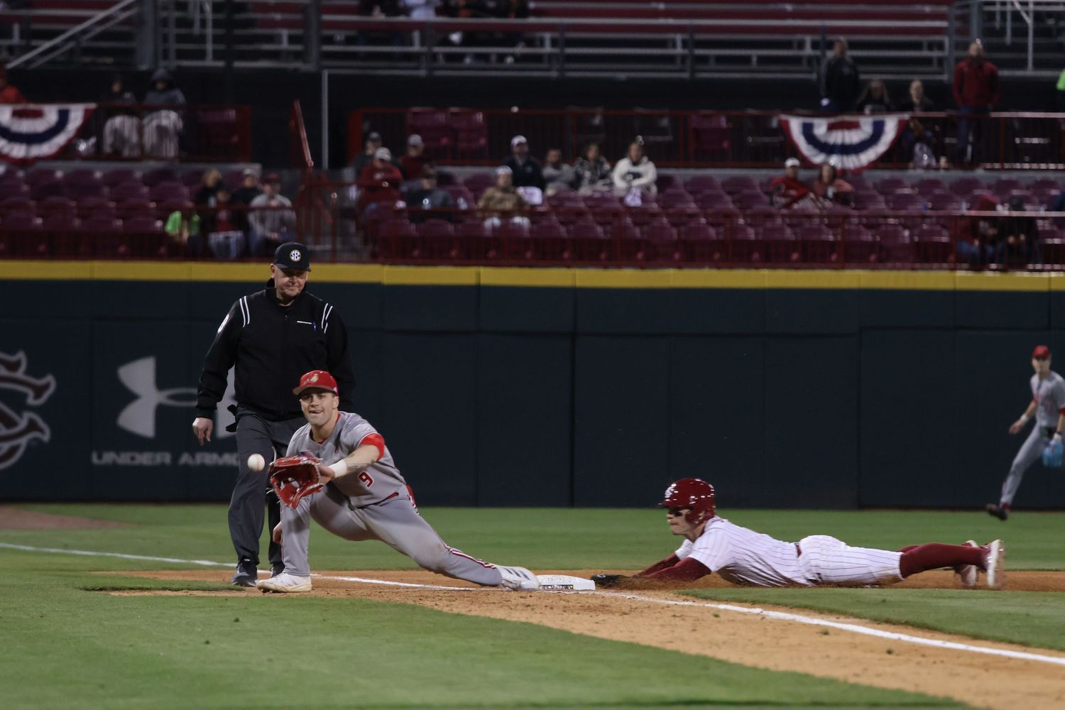South Carolina first baseman stretches for a throw while a runner dives back to the bag.