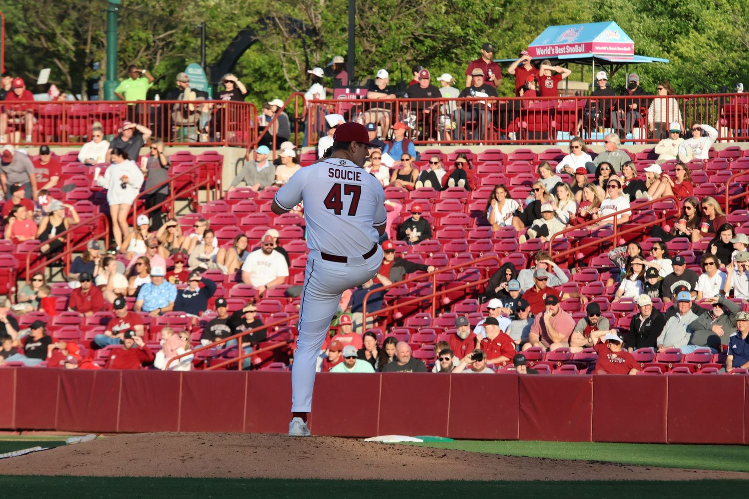 College baseball pitcher wearing number 47 stands on the mound with fans behind him.