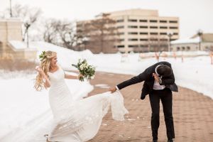 Bride and groom share a romantic winter wedding moment on a snowy brick path, with bride holding a white bouquet.