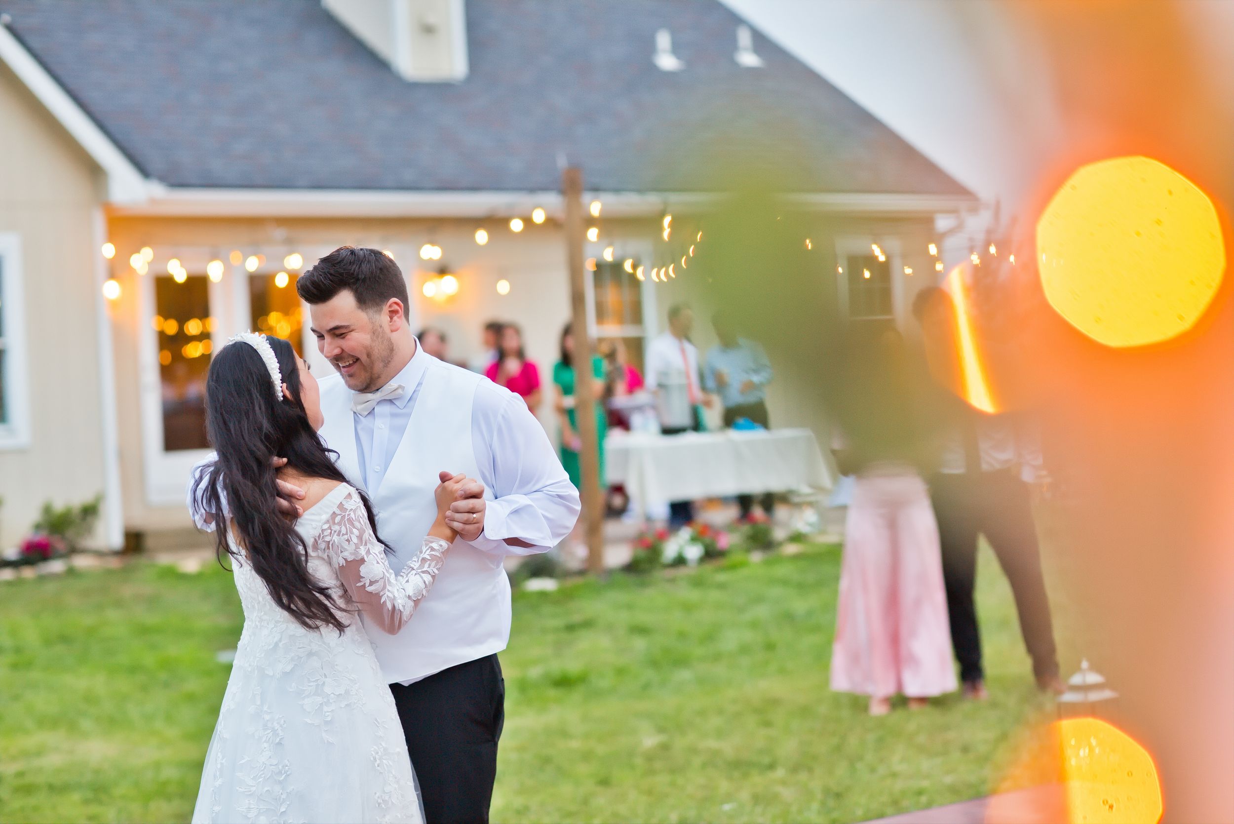 Newlyweds share their first dance outdoors at a backyard reception with warm string lights glowing.