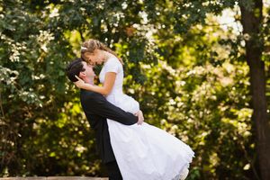 Groom sweeps bride off her feet for a kiss in a sunlit outdoor garden wedding photo.
