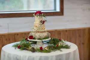Elegant three-tier semi-naked wedding cake decorated with red roses and greenery on a white tablecloth.