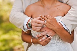 Close-up of bride and groom exchanging wedding rings, groom wearing a watch and black band.