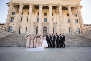 Wedding party posing on grand stone steps of neoclassical building with bridesmaids in blush gowns.