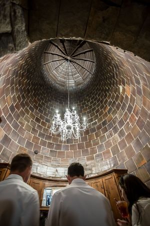 Wedding guests admire a stunning domed brick ceiling with chandelier in a historic venue.