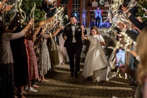 Bride and groom exit through a sparkler tunnel surrounded by cheering wedding guests at night.