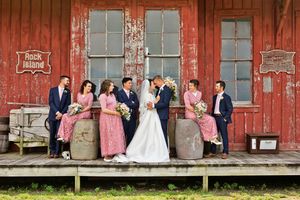 Wedding party posing on rustic red barn porch at Rock Island with bride and groom kissing.