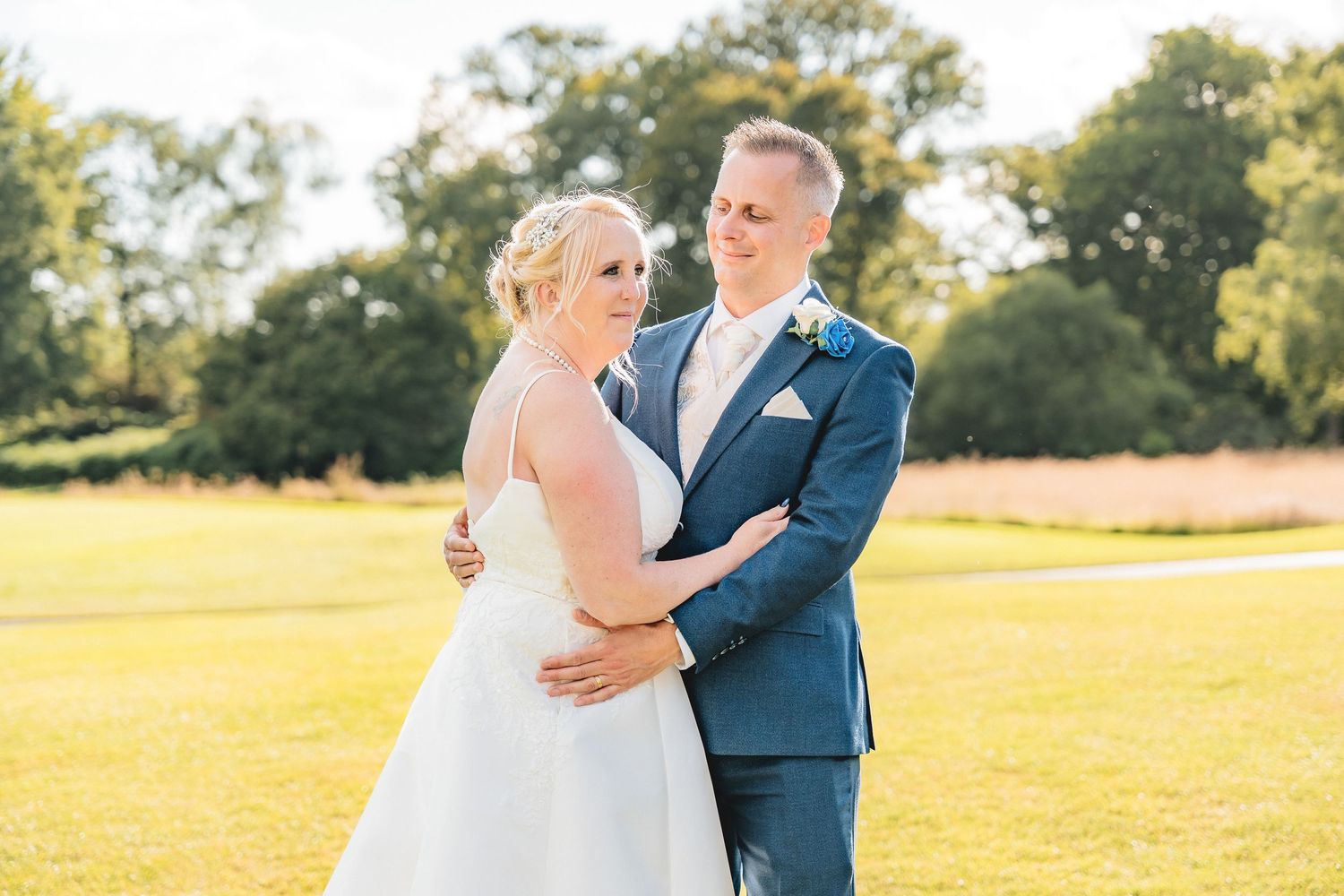 A romantic wedding portrait taken in a sunlit field with a couple embracing in formal attire.
