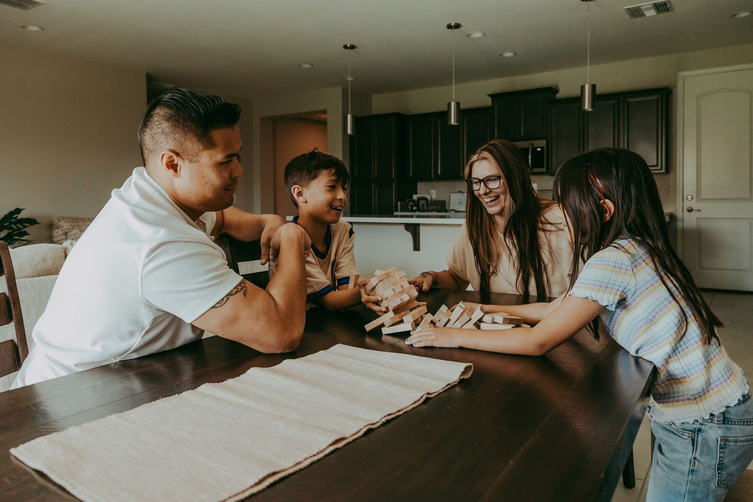 Family of four playing a board game together at a dining table in a cozy home kitchen setting. Surprise, Arizona