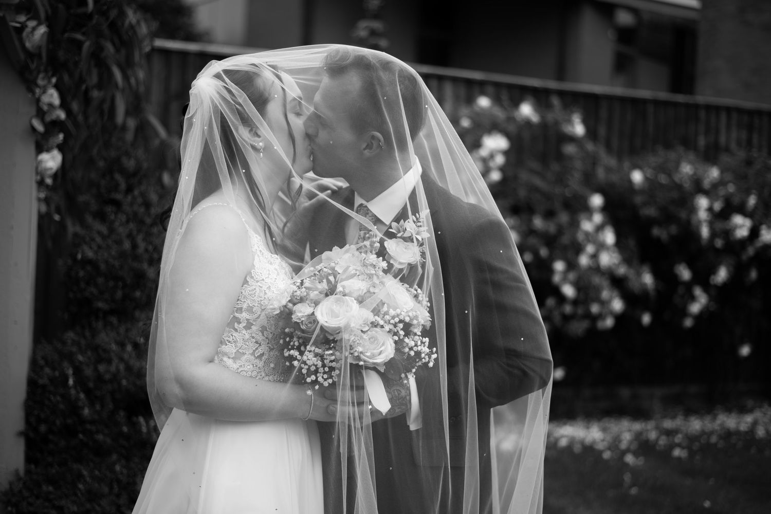 A romantic wedding couple shares intimate kisses under a flowing veils in golden sunlight.