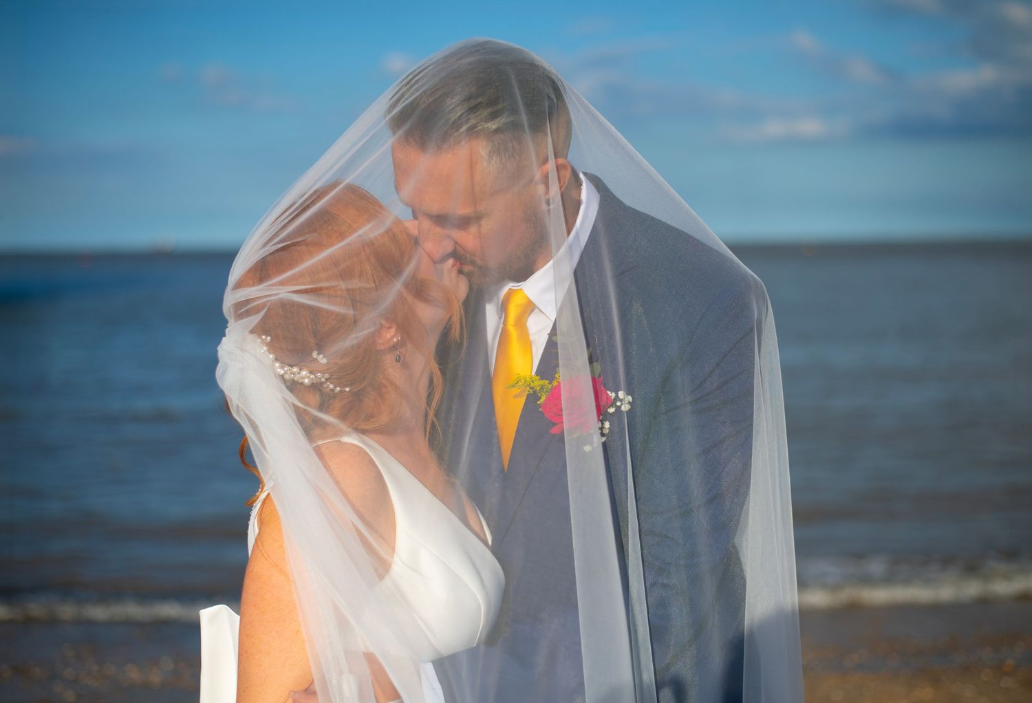 A romantic wedding couple shares intimate kisses under a flowing veils in golden sunlight.