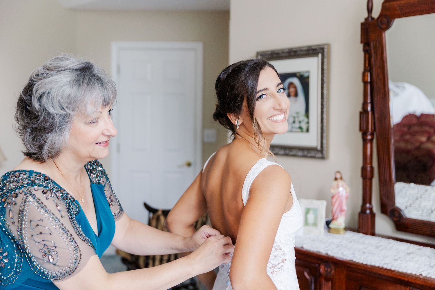 Wedding preparation scene with two people at a vintage wooden vanity mirror.