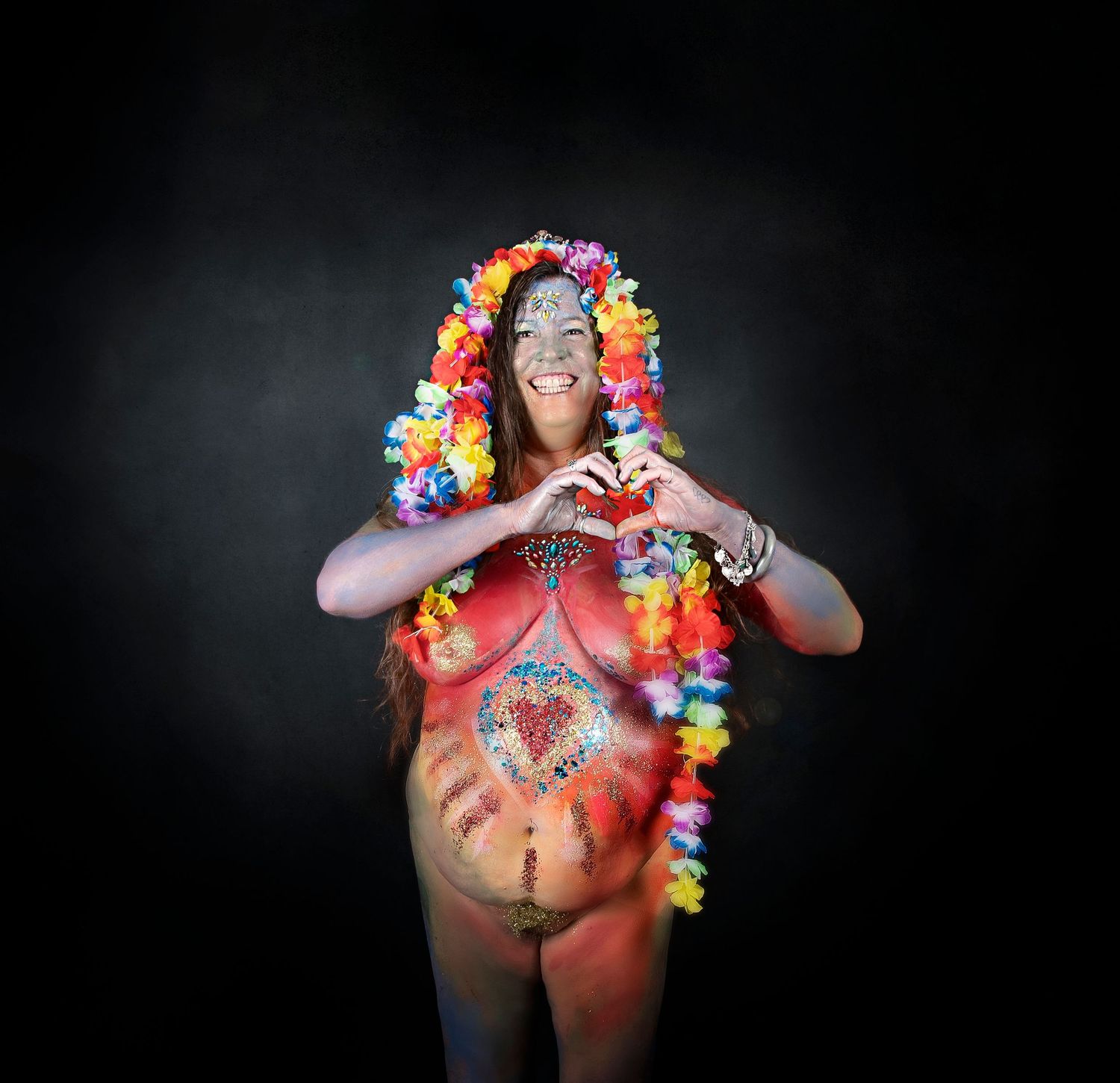 A woman wearing a colorful lei and body paint poses against a dark background in an artistic portrait.