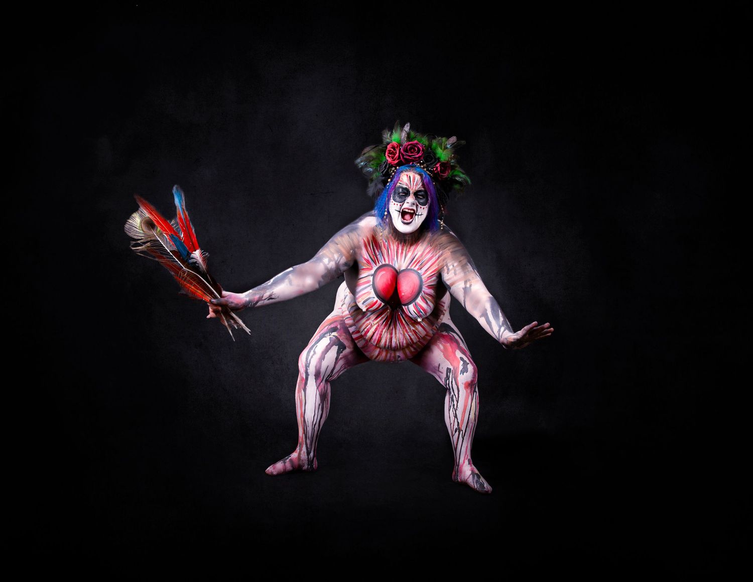 A Witch in white body paint and dark crown poses dramatically against black background with blood-red accents.