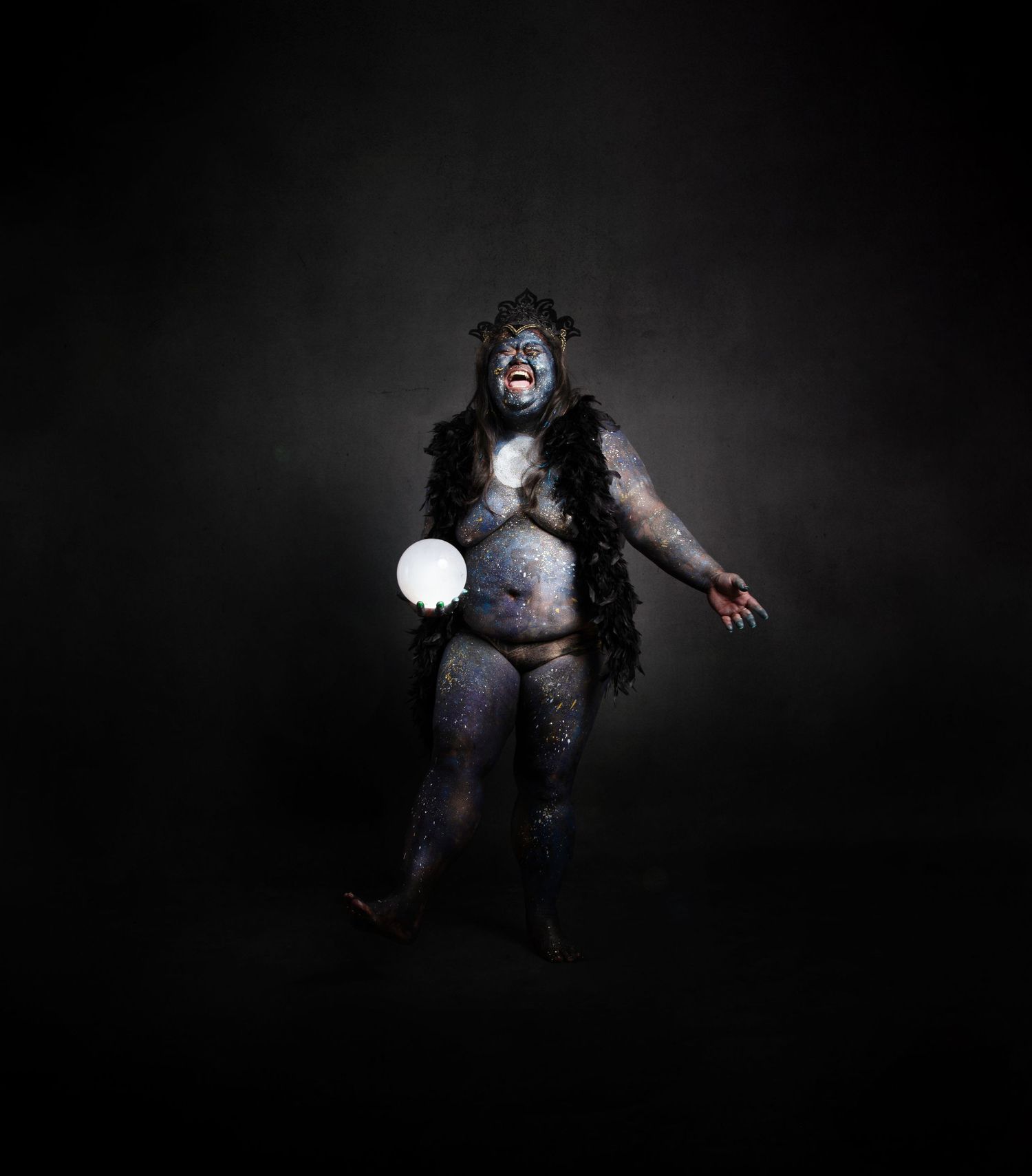 Moon Goddess in a dark costume holds a glowing orb while floating dramatically against a black background.