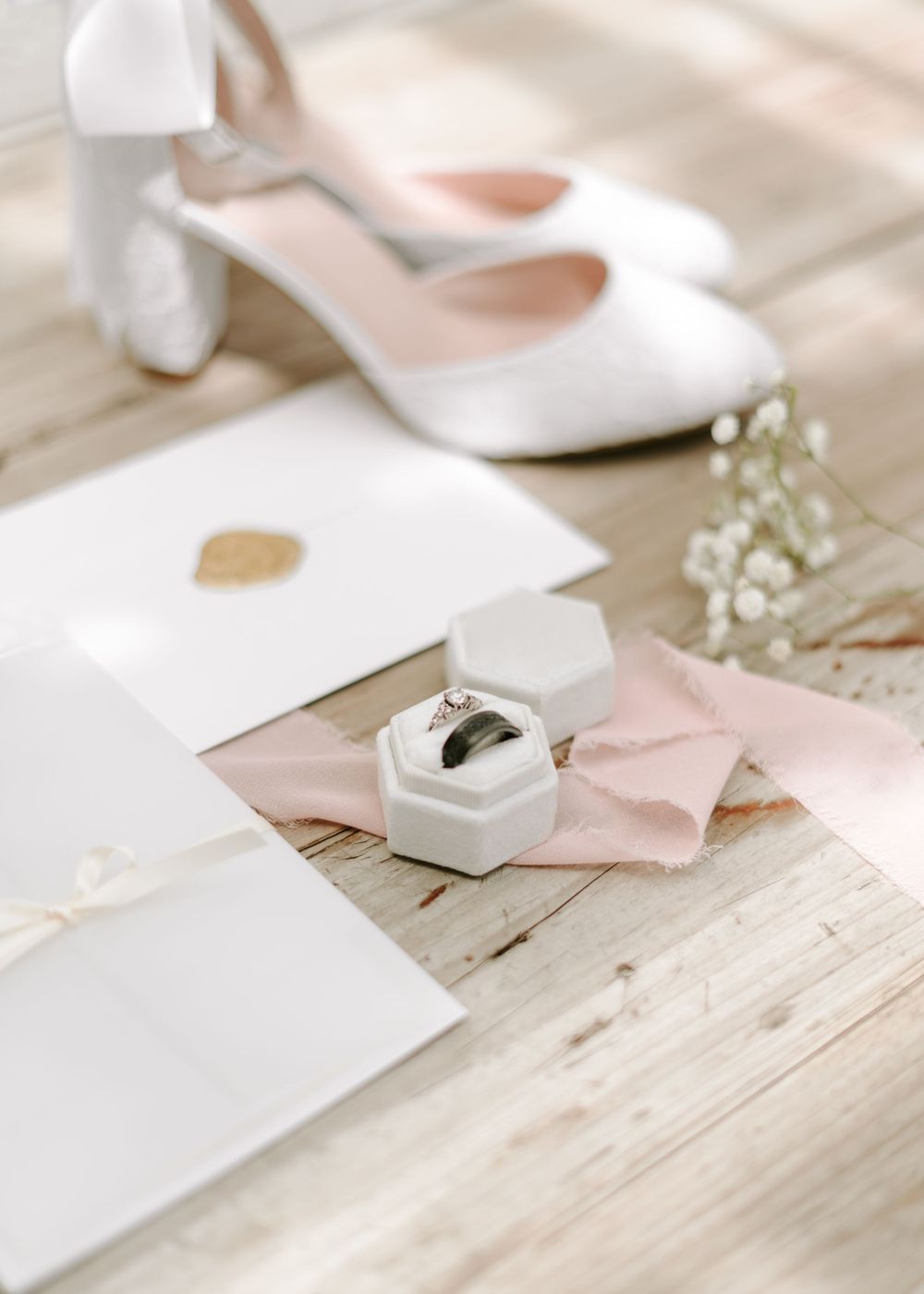 Wedding details with white shoes, stationery, and a ring box on a rustic wooden surface.