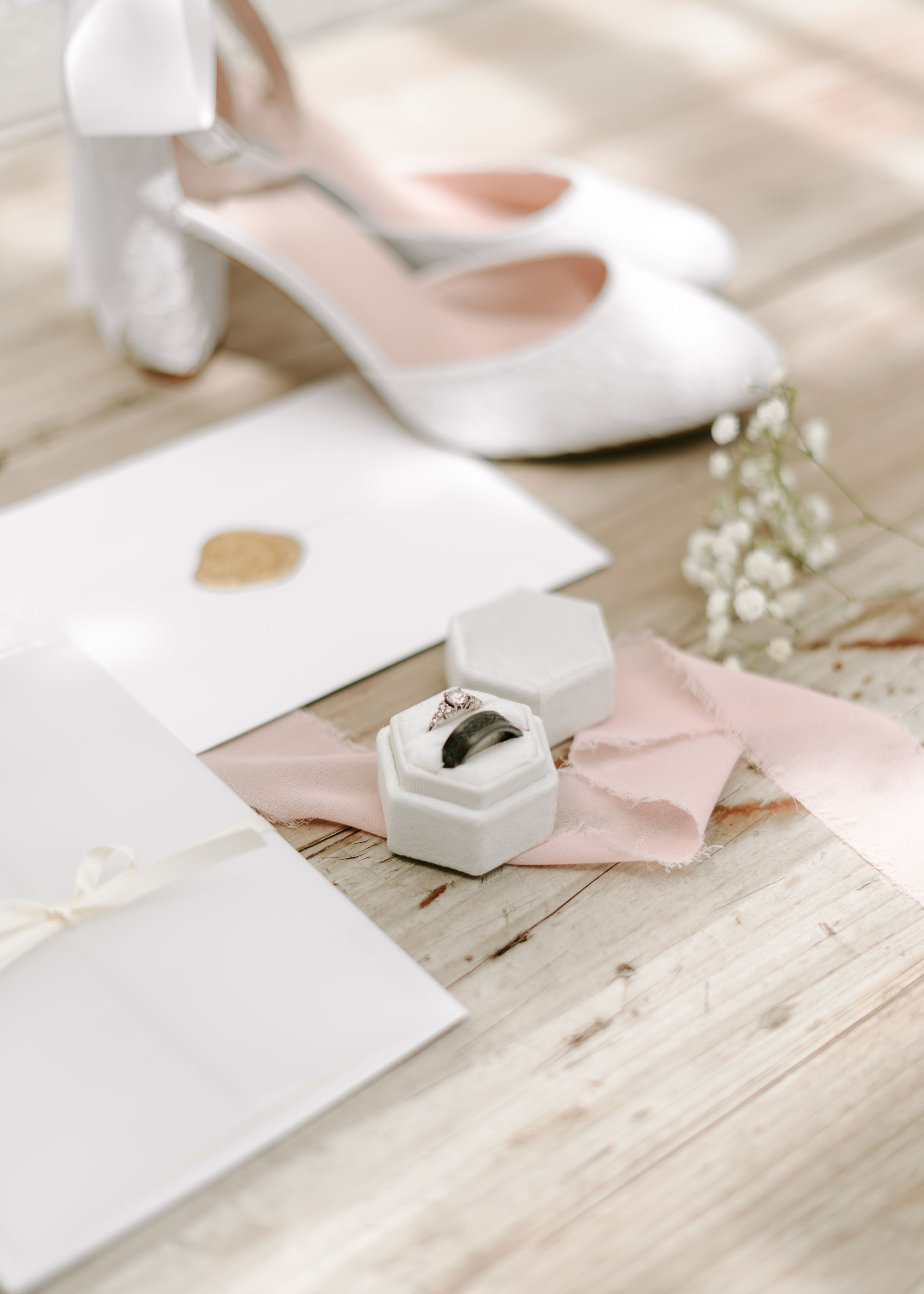 Wedding details with white shoes, stationery, and a ring box on a rustic wooden surface.