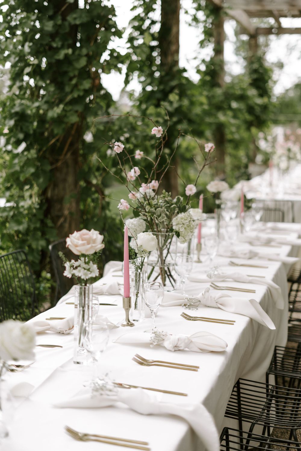 Elegant wedding table setting with delicate pink flowers in glass vases and gold flatware.
