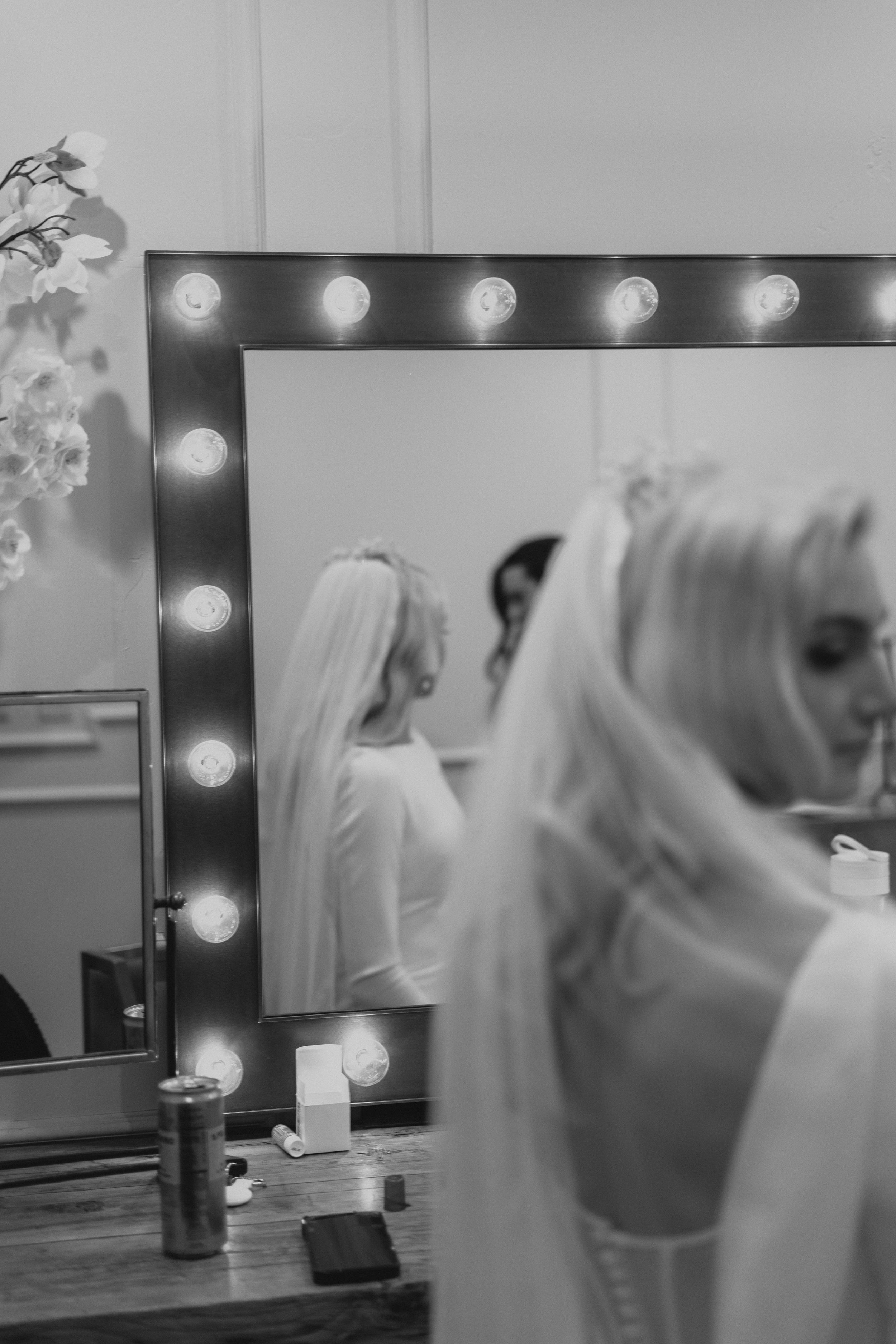 Black and white image of a makeup vanity with illuminated mirror and wedding preparations.