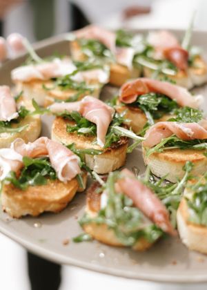 Elegant appetizers with prosciutto and arugula served on toasted crostini.