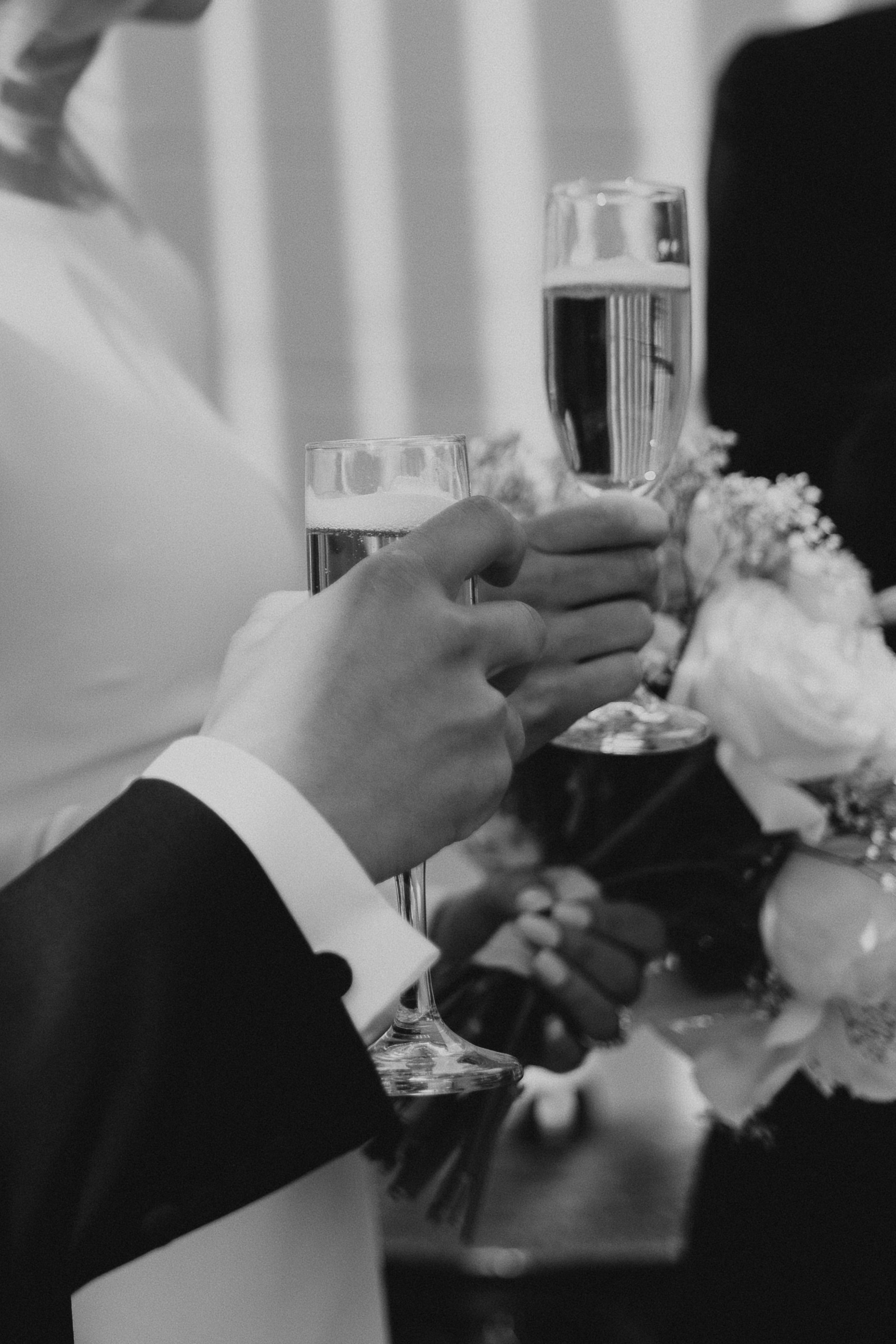 Black and white photo of champagne glasses being toasted at a wedding celebration.