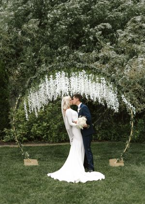 Wedding ceremony under a beautiful white floral arch in a garden setting.
