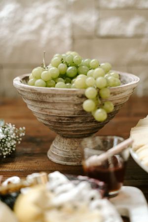 Fresh green grapes displayed in a rustic wooden bowl on a wooden table.