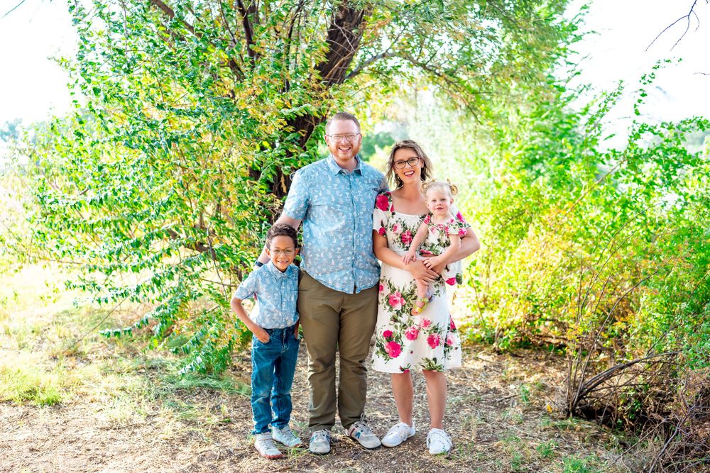 Family of three poses together outdoors wearing coordinated floral and blue outfits.