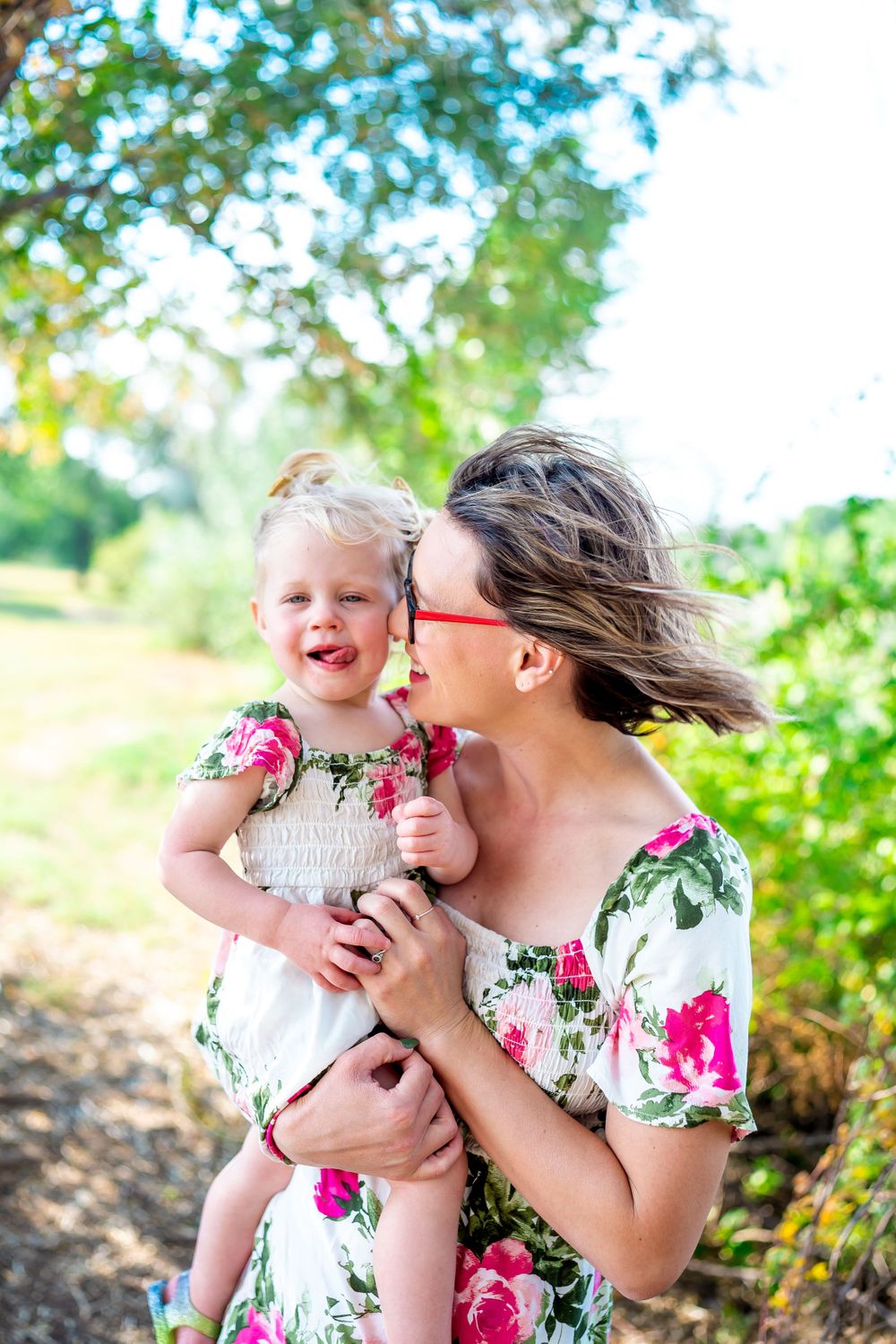Mother and child in matching floral dresses share a tender moment outdoors.