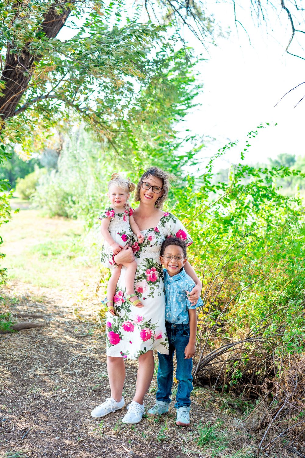Family photo in a garden setting wearing coordinated floral and blue outfits on a sunny day.