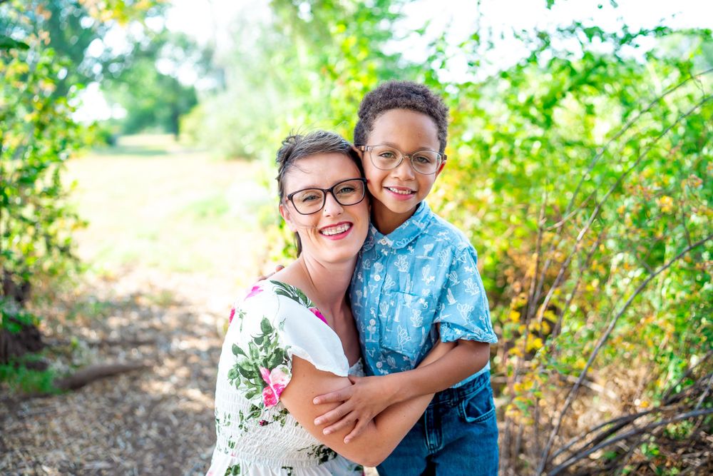 Outdoor portrait of parent and child embracing and smiling in natural lighting.