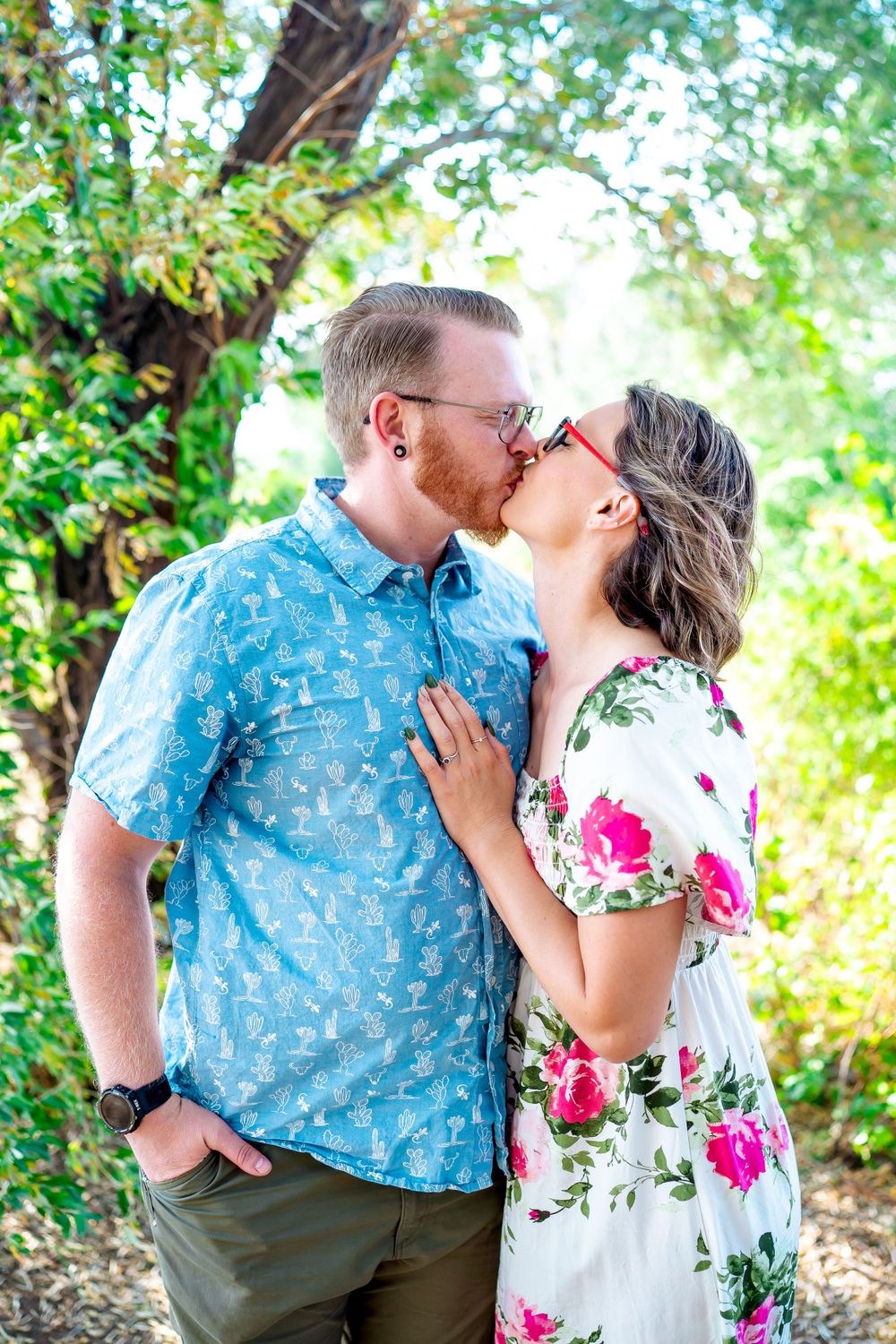 Romantic couple sharing a kiss while wearing coordinated outfits in a sunny outdoor setting.