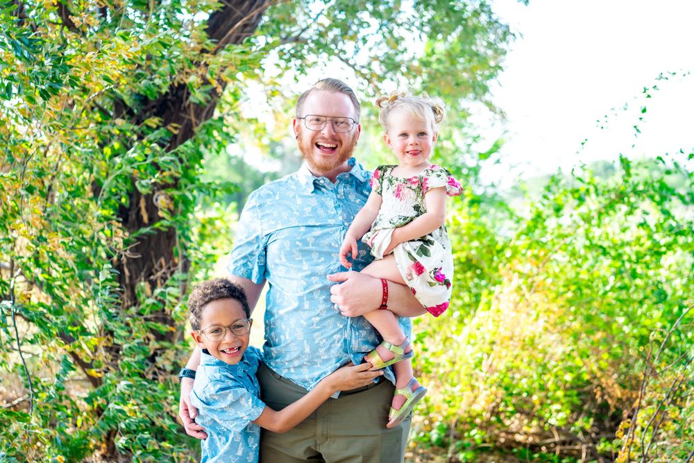 Family group portrait outdoors with matching blue shirts and natural background.