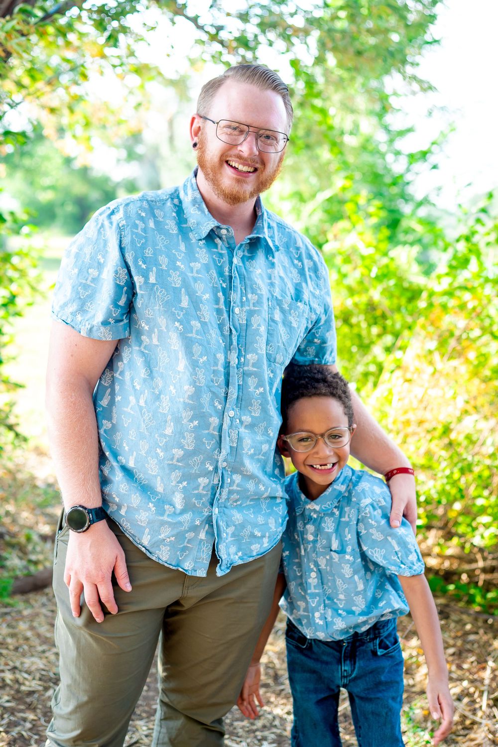Parent and child in matching blue patterned shirts smile together on nature trail.