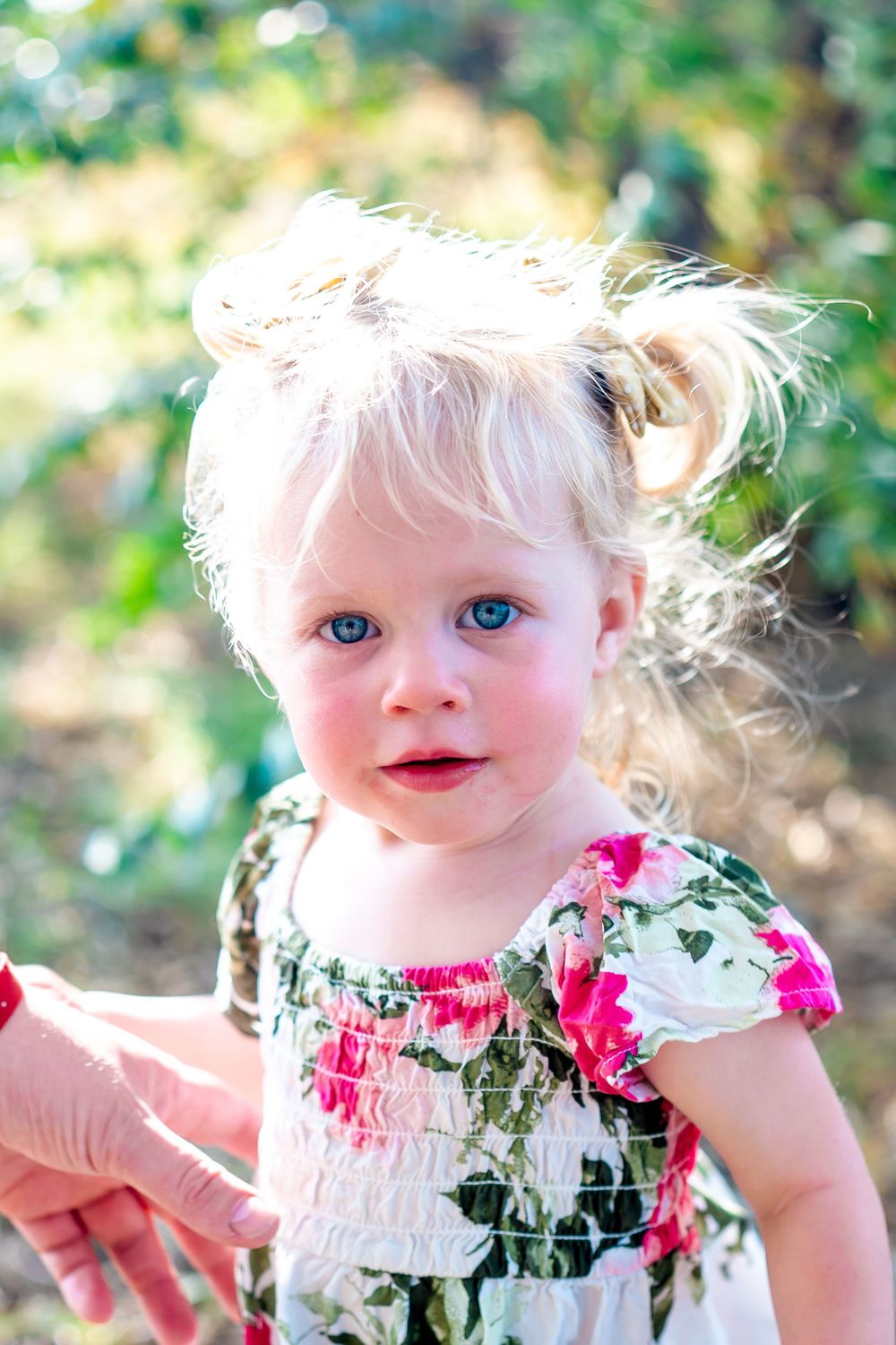 Young child with blonde hair wearing floral dress smiles in natural outdoor lighting.