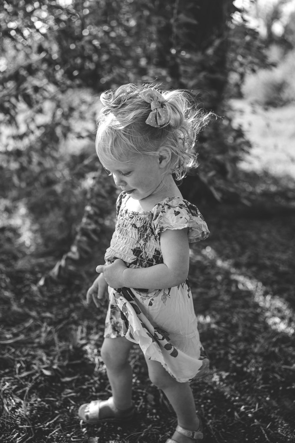 Black and white portrait of toddler in floral dress playing outdoors.