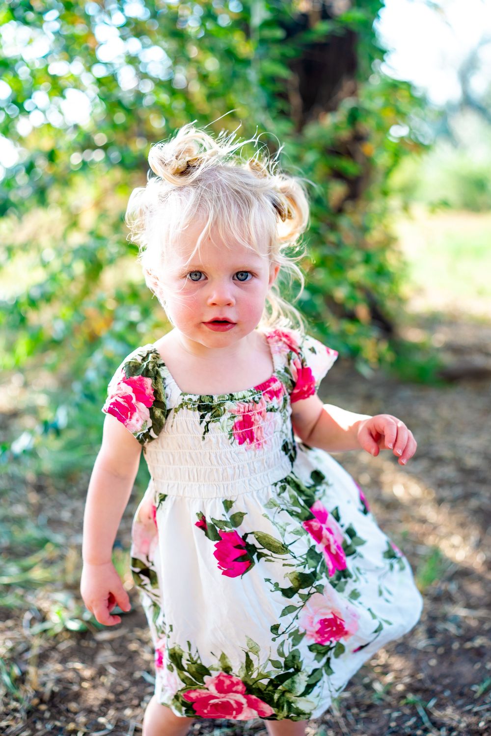 A floral sundress with pink roses on a white background is worn in a garden setting.