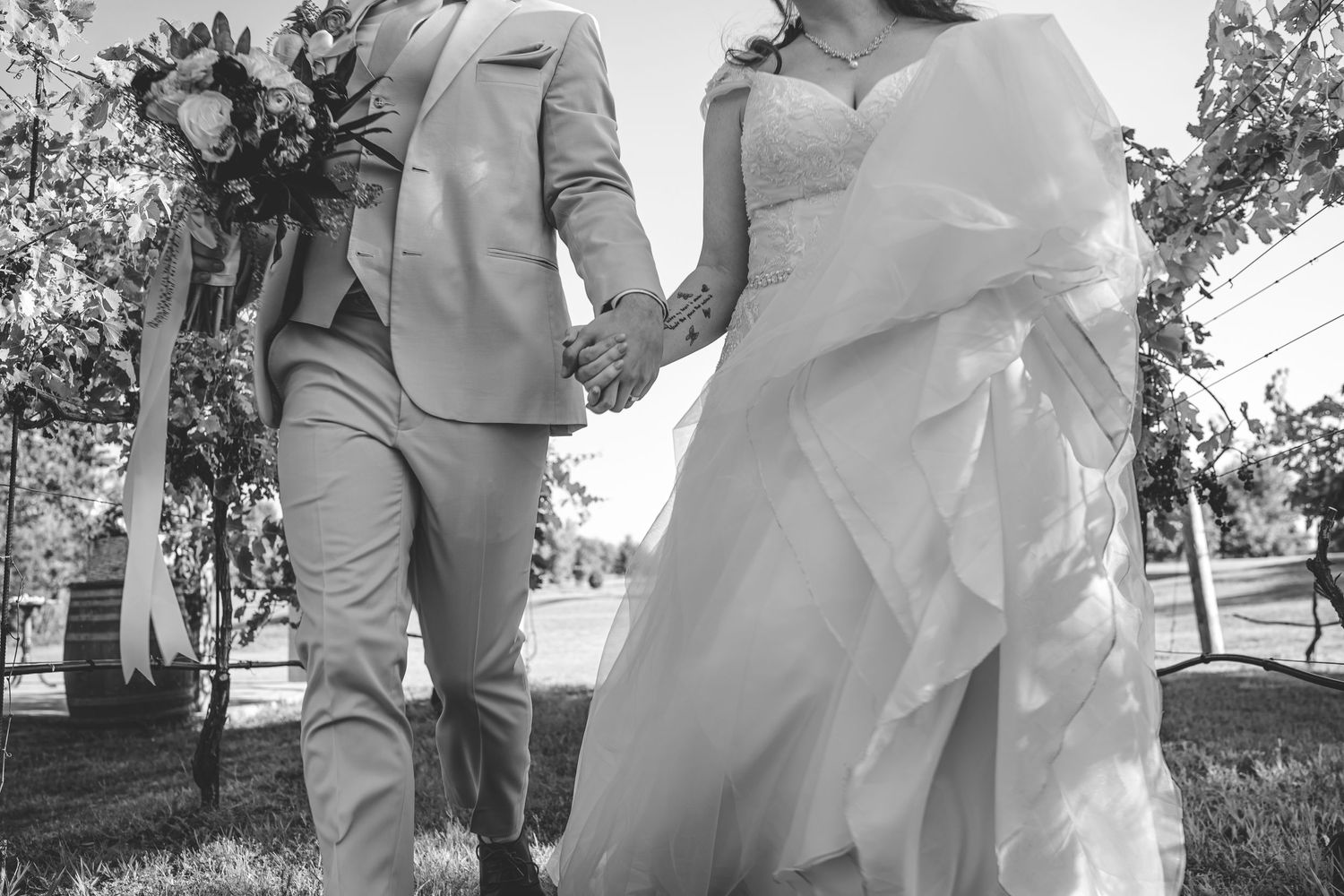 A black and white photo of a couple walking hand in hand on their wedding day.