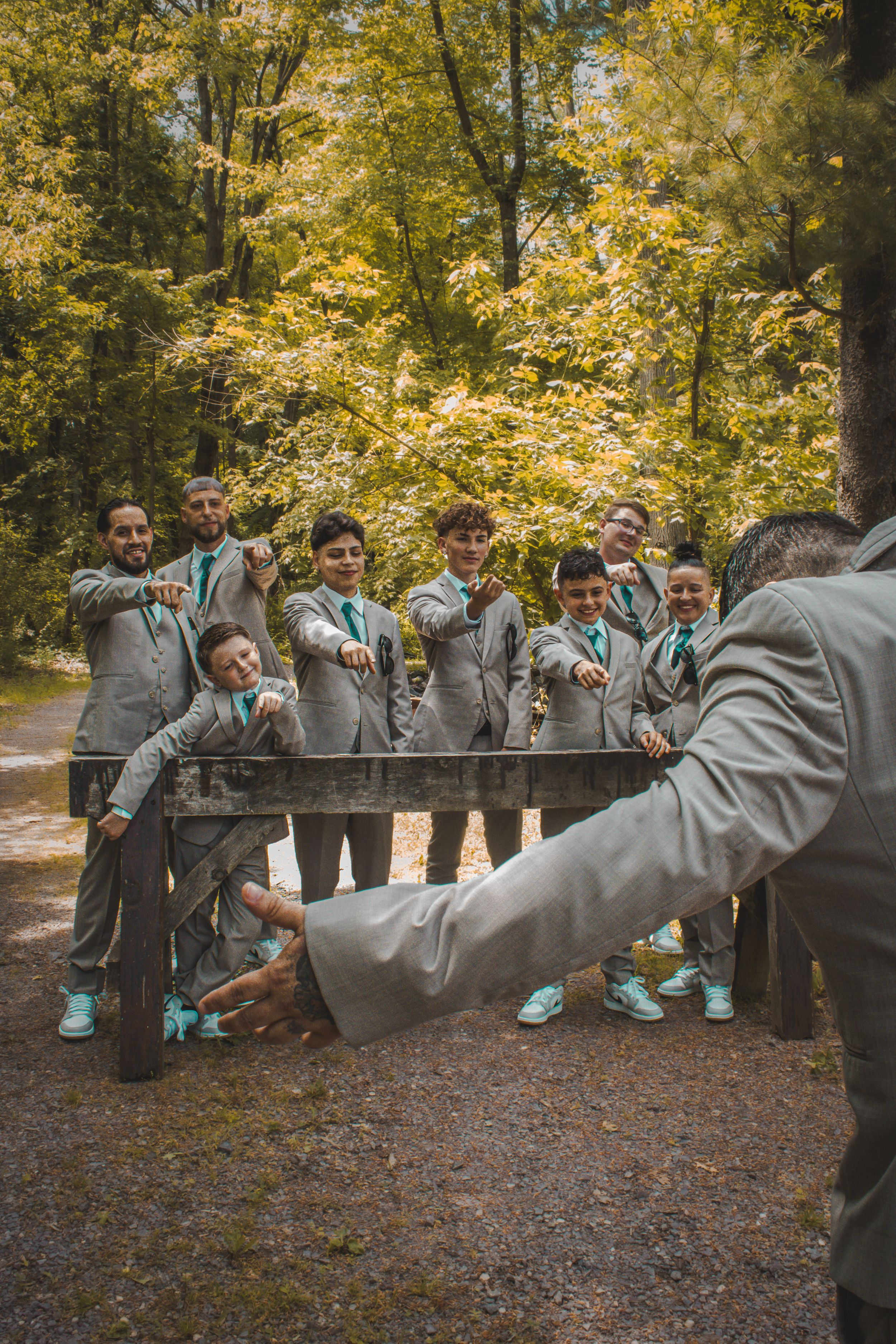 Groom standing in a woodsy location, facing his bachelor party, all the bachelors laughing and joking with him in a playful moment.