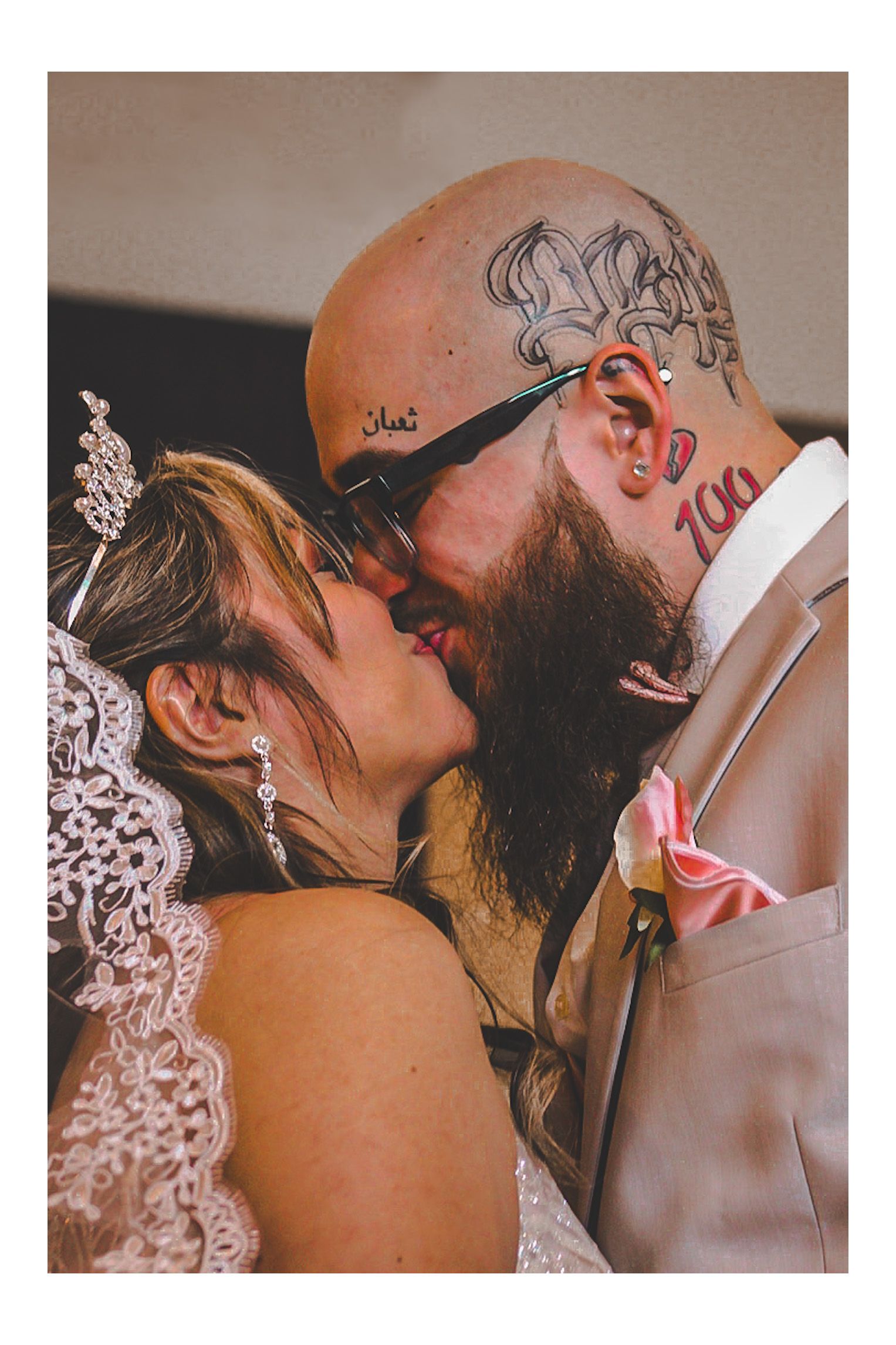 A wedding couple is sharing their first kiss.  The bride is wearing a veil and the groom is wearing glasses and tuxedo.