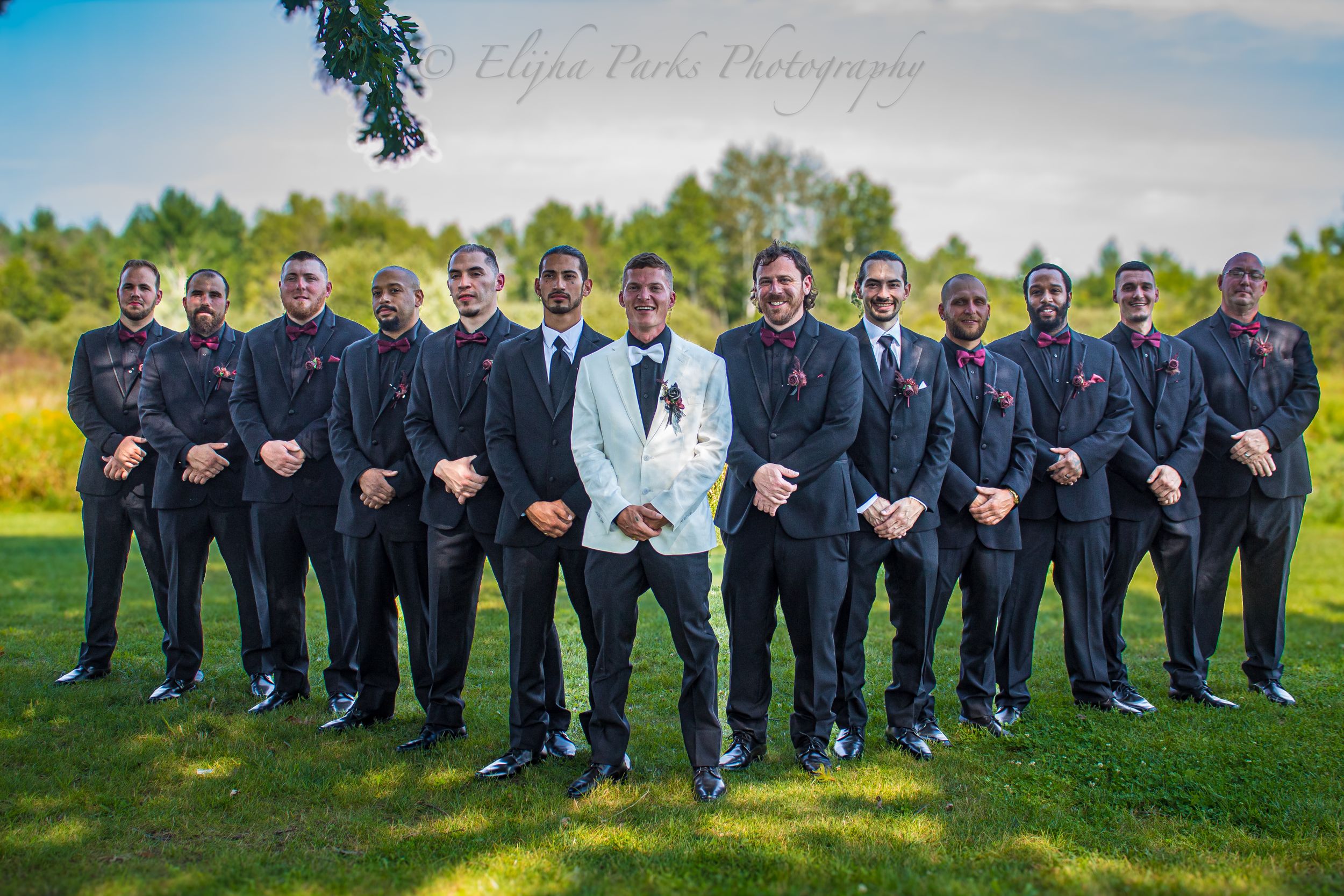 groom is standing in the middle of his groomsmen.  There are twelve groomsman. All men are in wedding attire.